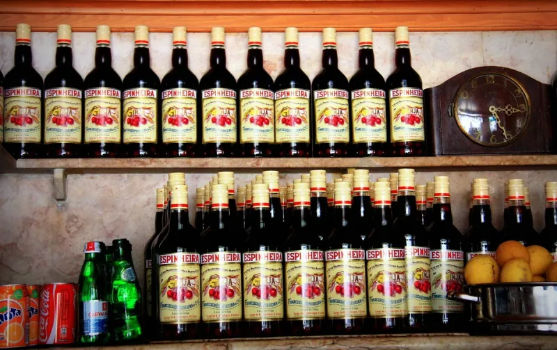 Wooden shelves packed with identical cherry liqueur bottles beside an old clock