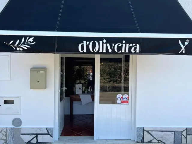 A white facade with a black awning, an open entrance door and a display window beside it