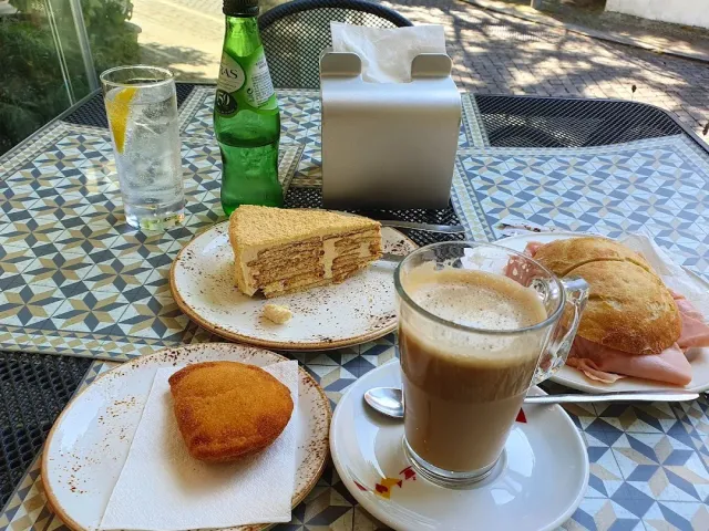 A glass of latte, a slice of cake and a sandwich on a tiled courtyard table