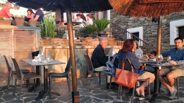 A terrace with straw parasols and stone walls, diners seated in afternoon light