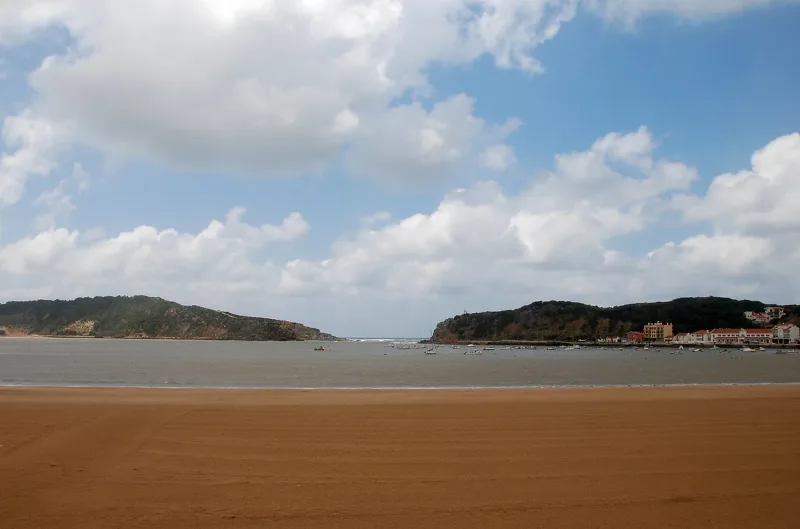 Almost enclosed bay between two green headlands with a broad sweep of sand in front