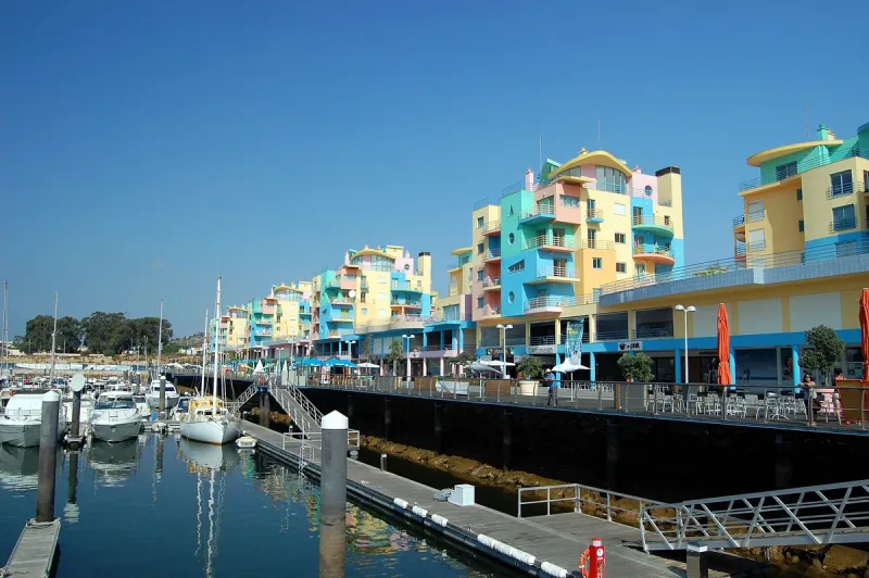 Marina of white yachts beside quayside buildings painted yellow, blue and pink