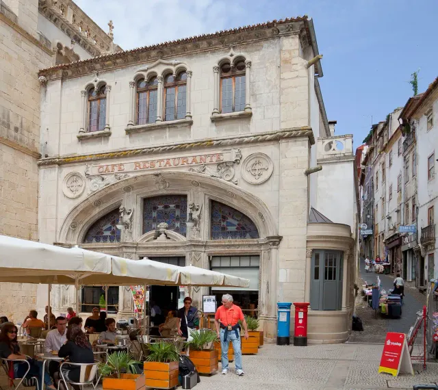 The arched stone front of a former chapel with a shaded cafe terrace