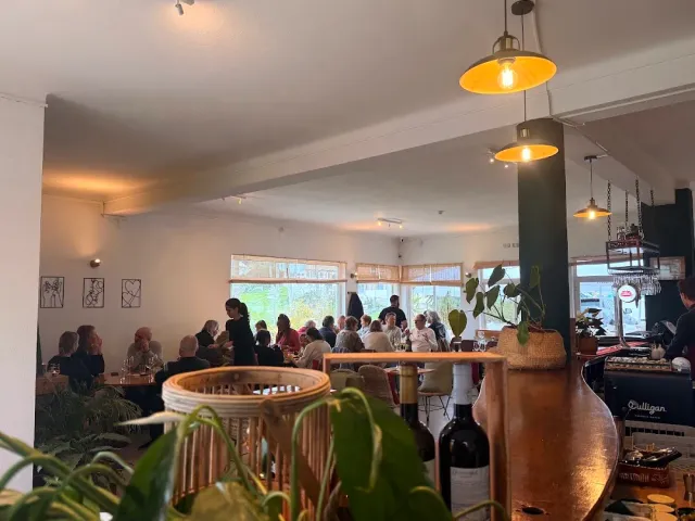 A space full of diners with hanging brass lamps, a wooden counter and greenery in the foreground