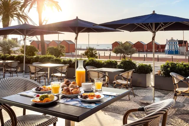 A breakfast table with pastries and juice under blue parasols facing the sea