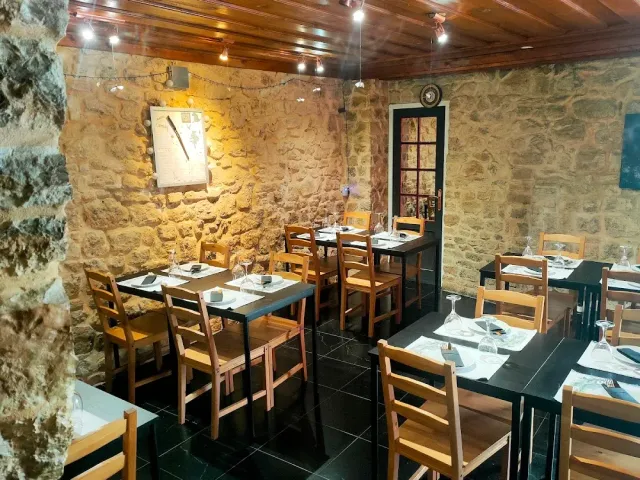 A room with stone walls, a wooden ceiling and dark tables with light chairs
