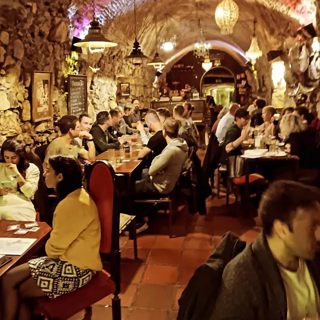 A vaulted stone cellar full of diners at wooden tables, under chandeliers
