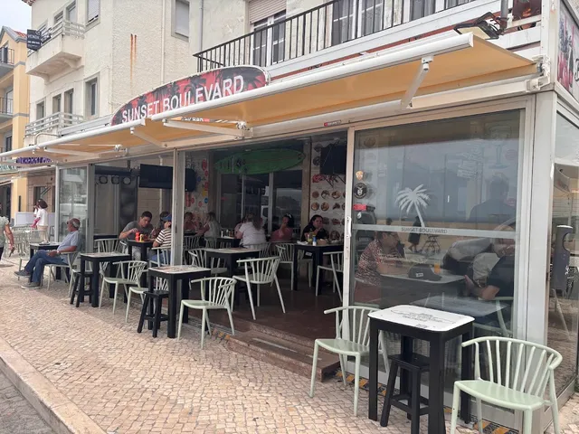 A pub front with a yellow awning and tables on a cobbled stone pavement