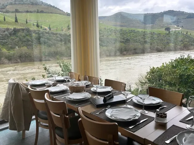 A long set table facing a picture window onto a river and terraced vineyard hills