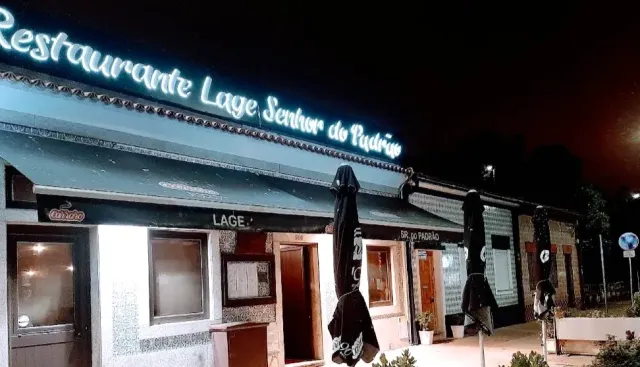 A facade lit at night with a white neon sign and closed parasols in front of it