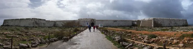 A long low fortress wall with a single entrance gate above a cliff plateau