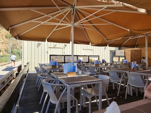A wooden deck with tables and white chairs under large brown umbrellas