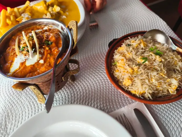 A metal bowl with orange curry and cream, beside a bowl of spiced rice and fries