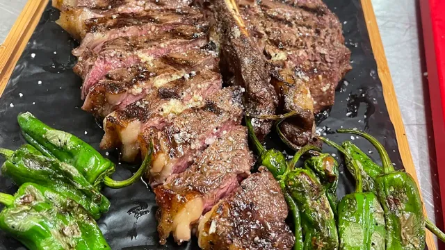 A grilled sliced steak on a dark board with fried green peppers