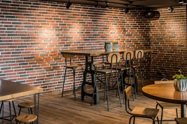 An empty space with a red brick wall, high tables, metal stools and track lighting