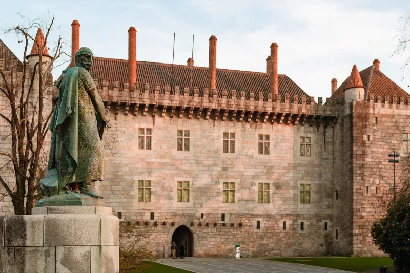 A stone palace with dozens of red brick chimneys and a bronze statue in front