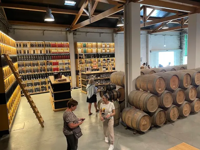A large sales hall with lit bottle shelves, stacked barrels and visitors