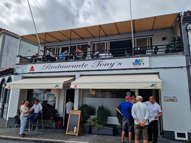 A two storey white building with diners on the upper balcony and people at the entrance