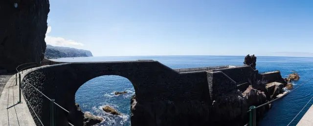 A dark basalt pier with an open arch above blue water and rocks