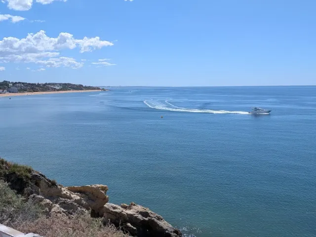 A blue sea with a motorboat leaving a wake, and a cliff rock in the foreground