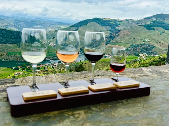 Four wine glasses on a tasting board, facing terraced vineyard hills and a river