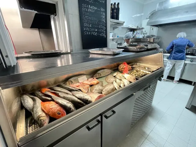 A chilled counter with fresh fish, a chalk price board and an open kitchen behind