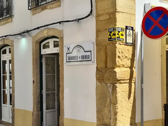A white facade in an alley with a narrow arched door, a hanging sign and a dressed stone corner