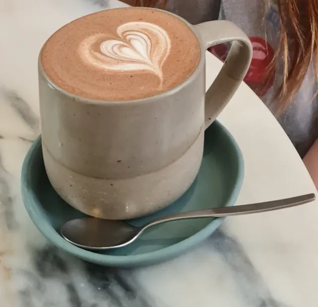 A ceramic mug with a heart drawn in the foam, on a light blue saucer and a marble table