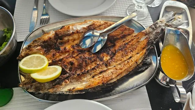 A whole grilled fish opened on a metal tray with lemon slices and sauce
