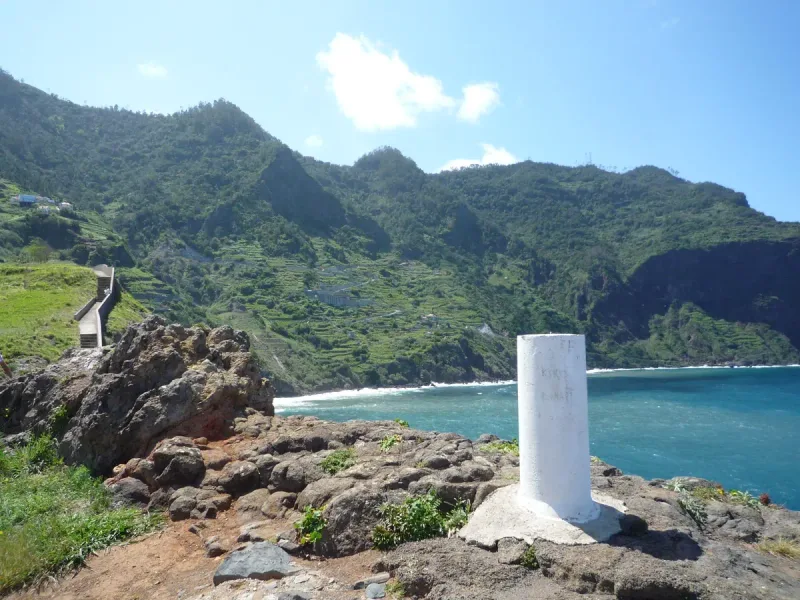 Rocky viewing spur above turquoise water facing steep green slopes cut with terraces