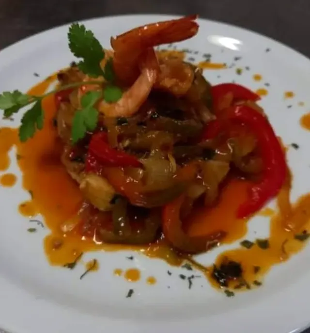 A white plate with prawns, red peppers and onion in an orange sauce, and coriander leaves