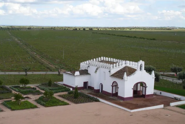 A white chapel with a crenellated gable and formal garden before vineyards to the horizon
