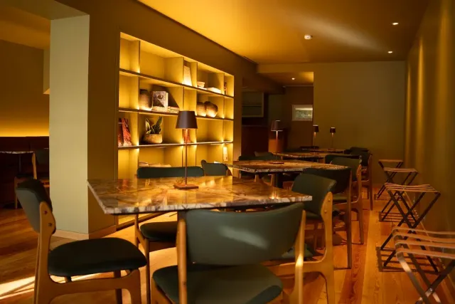 A warmly lit room with a marble table, green chairs and lit niches in the wall
