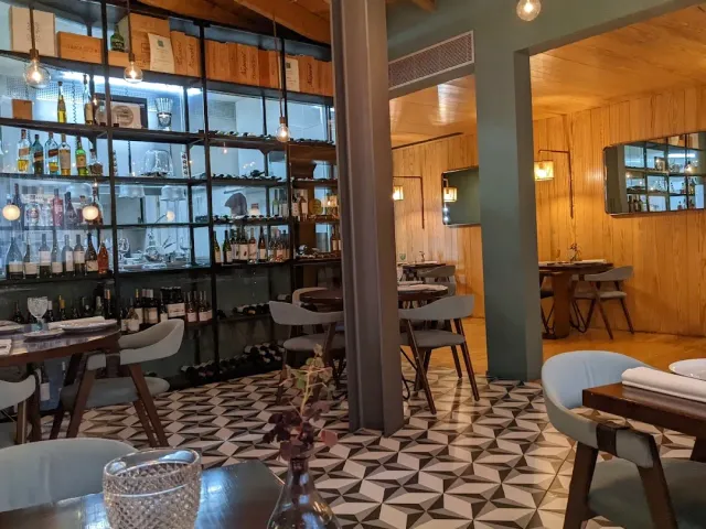 A glass shelving unit with bottles and vessels, a geometric tiled floor and small tables