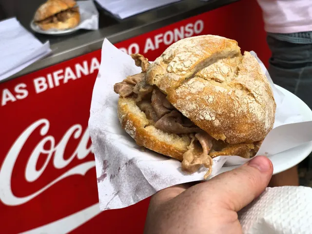A bread roll sandwich with sliced meat in paper before the venue's red sign
