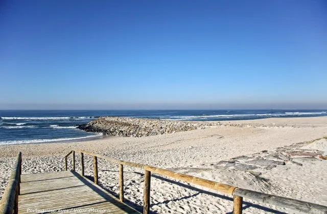 A wooden path down to a wide sandy beach with a breakwater and blue sea