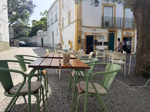 Green metal chairs and a wooden table in a paved square facing white houses