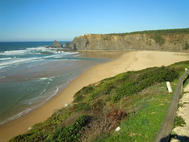 A sandy beach between high cliffs where a river meets the sea