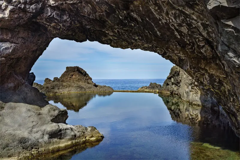 Dark volcanic rock arch opening onto a still pool with the ocean beyond