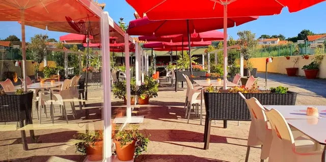 A paved terrace with red parasols, rattan chairs and flower pots in the sun