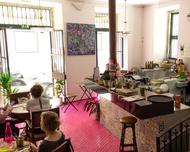A space with a vivid pink tiled floor, an abstract painting, chandeliers and a tile-clad counter