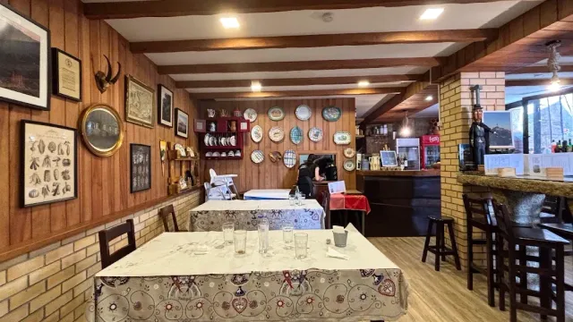 A rustic hall with wooden walls, embroidered tablecloths, hanging decorative plates and a beamed ceiling