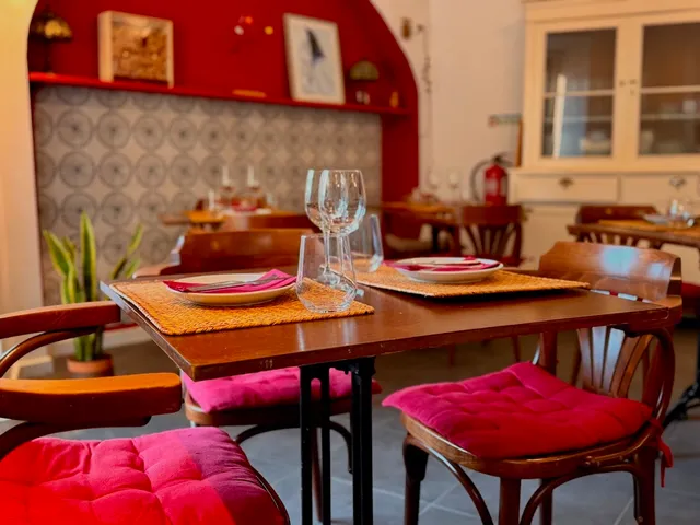 Small wooden tables with pink cushions in front of a tiled wall and a red shelf