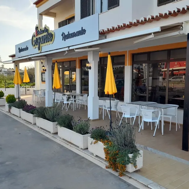 A white building with closed yellow parasols, white chairs and lavender planters