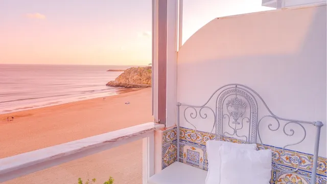A white balcony with a painted tile bench above a wide beach in pink sunset light