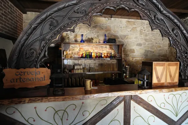 A bar in an antique style with a carved wooden arch, a stone wall and a shelf of colourful bottles