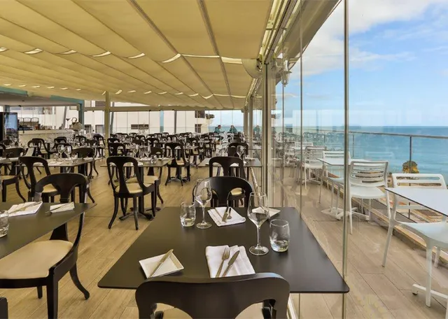 A covered dining hall with set tables and glass walls facing the sea