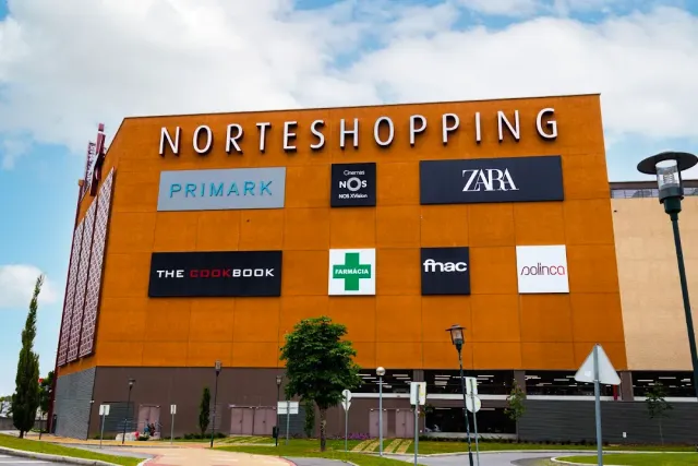 A tall orange mall facade with lit brand signs and a road in front