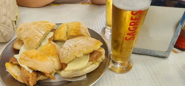 A metal plate with rolls filled with meat and cheese beside a glass of beer