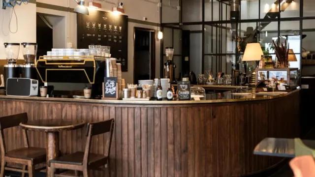 A curved wooden counter with an espresso machine, grinders, cups and chalkboards above it